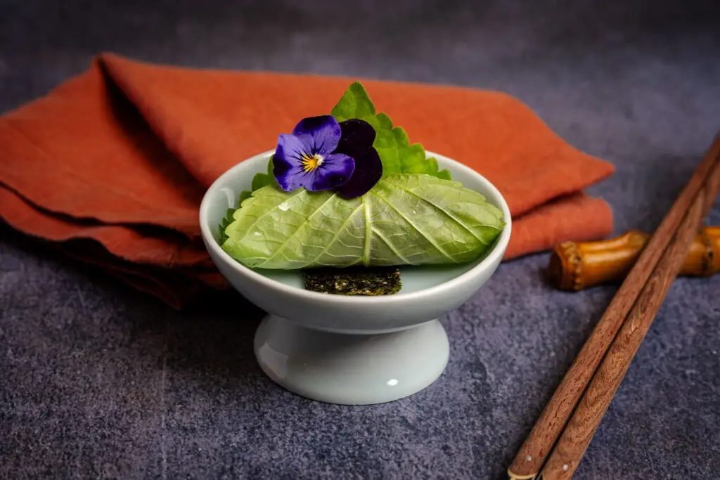 Leaf-wrapped dish with purple flower garnish