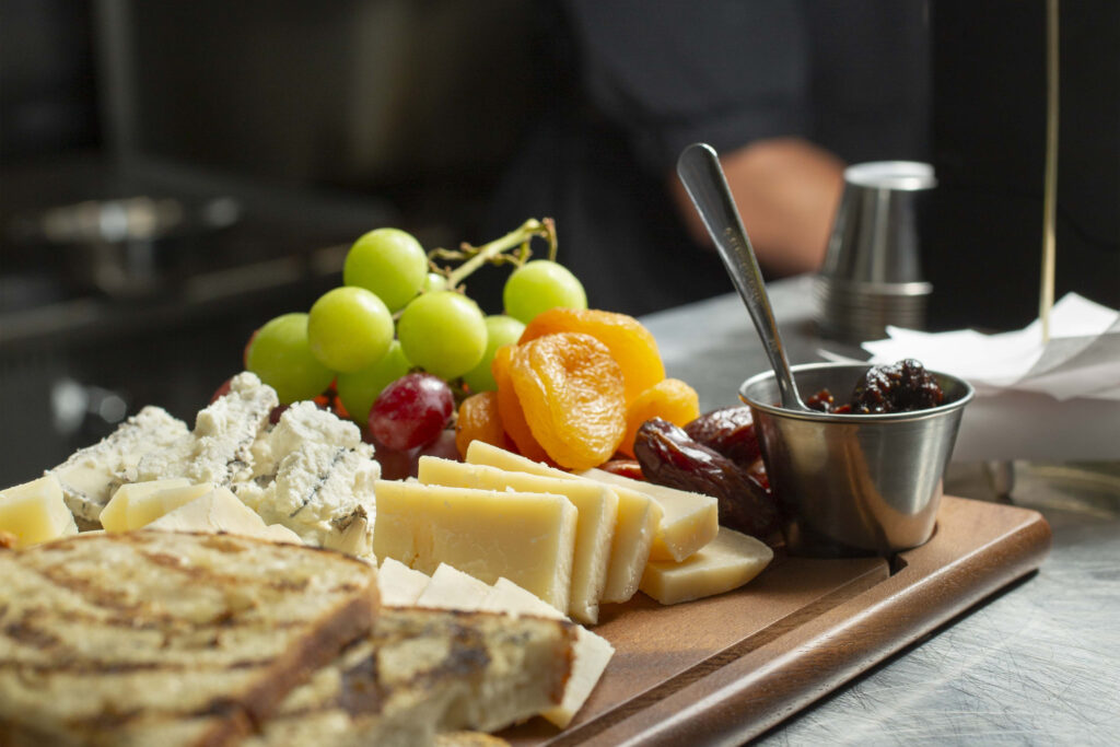 Cheese platter with fruits and preserves on a board.