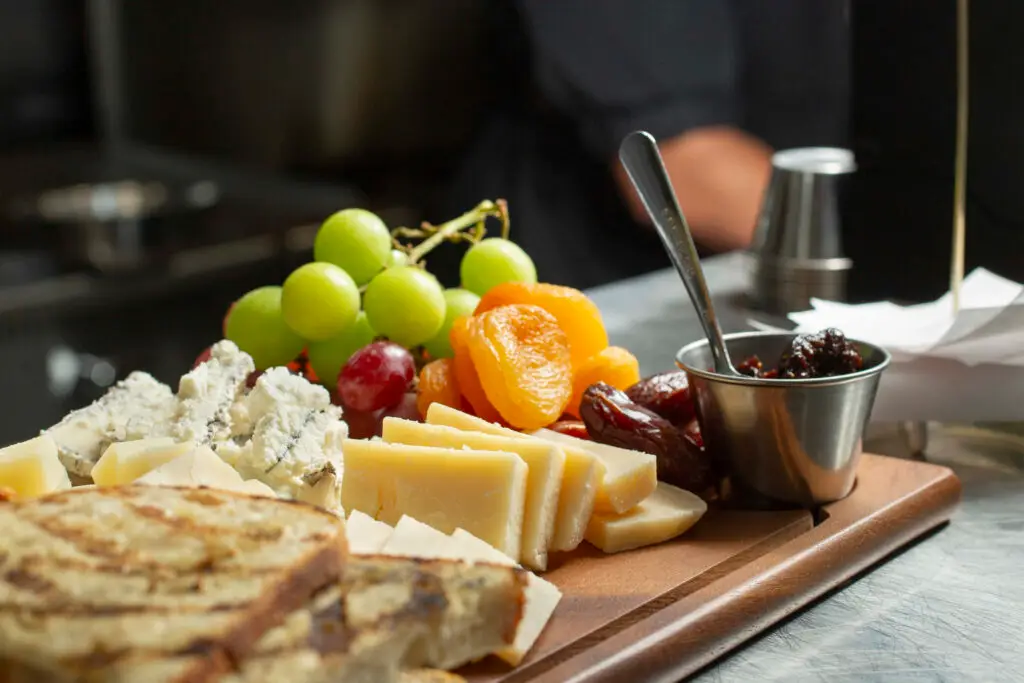 Cheese platter with fruits and preserves on a board.