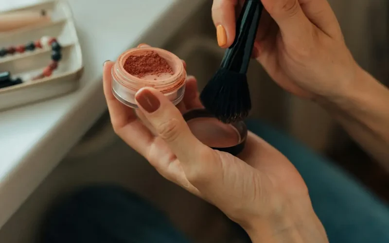 Applying makeup with brush at vanity desk.