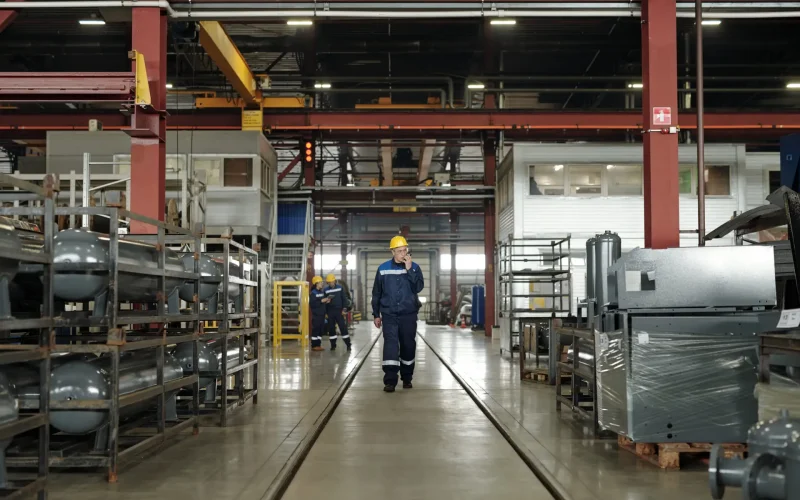 mature male worker of industrial plant using walkie talkie while moving along technical equipment